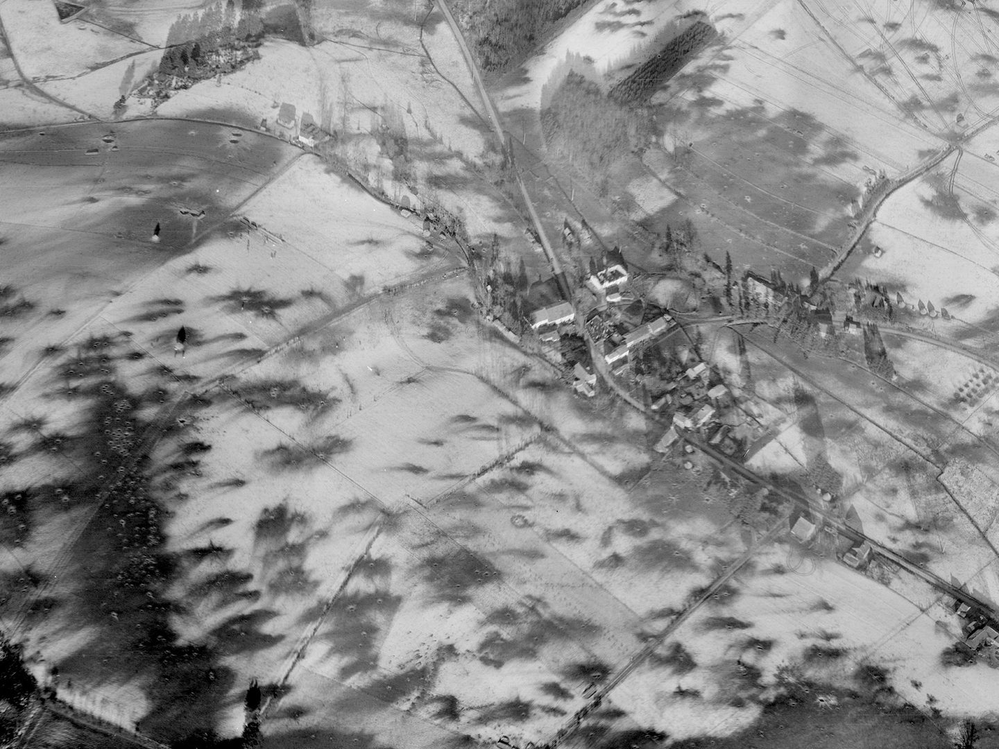 A historic black and white oblique aerial photo of a small village. The village and surrounding fields are covered with snow. Numerous bomb craters mark the snowy fields.