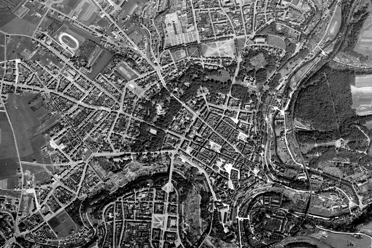 A historic black and white vertical aerial photo of the city of Luxembourg, showing the city radiating out from its centre, with a winding river running from bottom left to top right of the image.