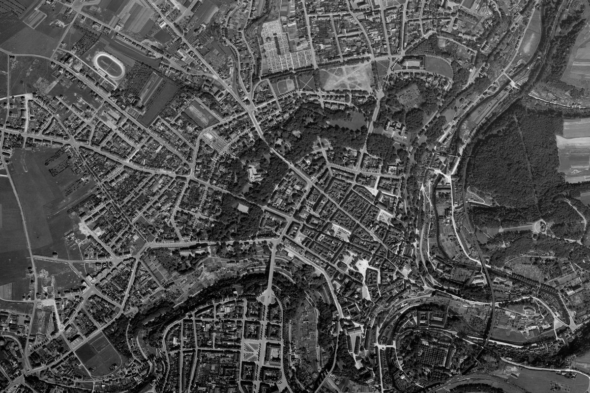 A historic black and white vertical aerial photo of the city of Luxembourg, showing the city radiating out from its centre, with a winding river running from bottom left to top right of the image.