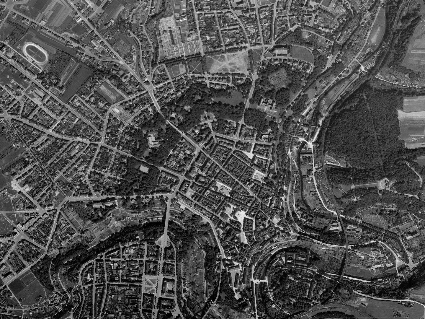 A historic black and white vertical aerial photo of the city of Luxembourg, showing the city radiating out from its centre, with a winding river running from bottom left to top right of the image.