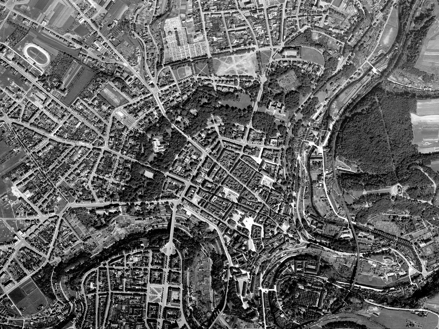 A historic black and white vertical aerial photo of the city of Luxembourg, showing the city radiating out from its centre, with a winding river running from bottom left to top right of the image.