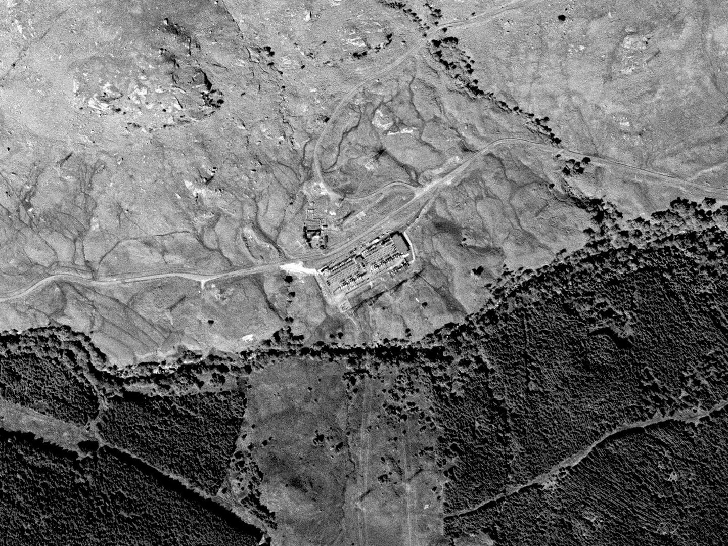 A historic black and white vertical aerial photo of a highland landscape. The upper portion of the image is moorland, with a wood along the lower portion. A large electricity transformer yard is visible in the centre of the image.