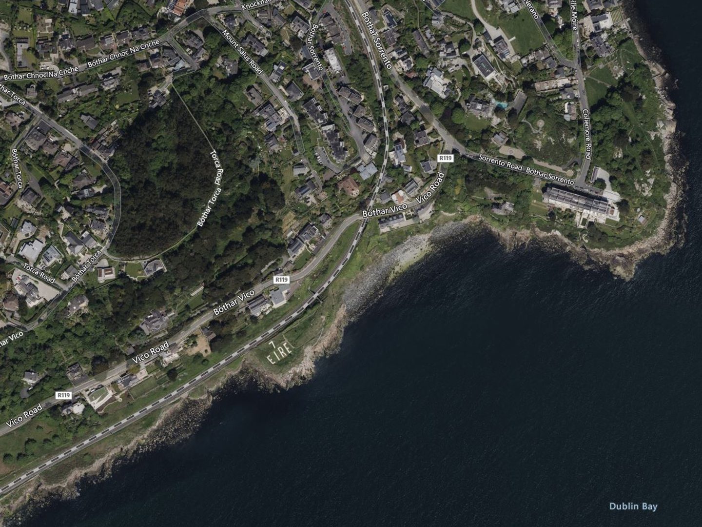 A contemporary colour satellite image of the same town and coastline as the previous image. The prominent field now clearly has the letters '7 EIRE' visible in white in it.