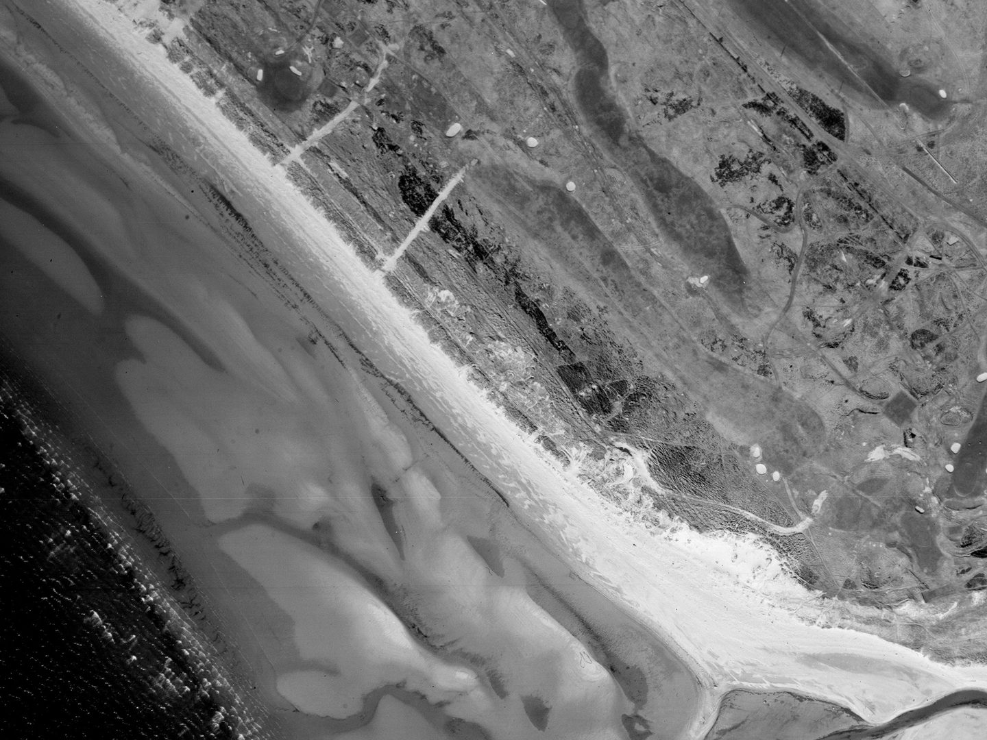 A historic black and white vertical aerial photo of a golf course running along the shore, with focus on a fairly long, straight hole running from top left to bottom right.