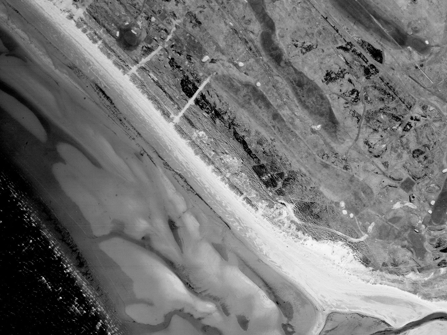 A historic black and white vertical aerial photo of a golf course running along the shore, with focus on a fairly long, straight hole running from top left to bottom right.