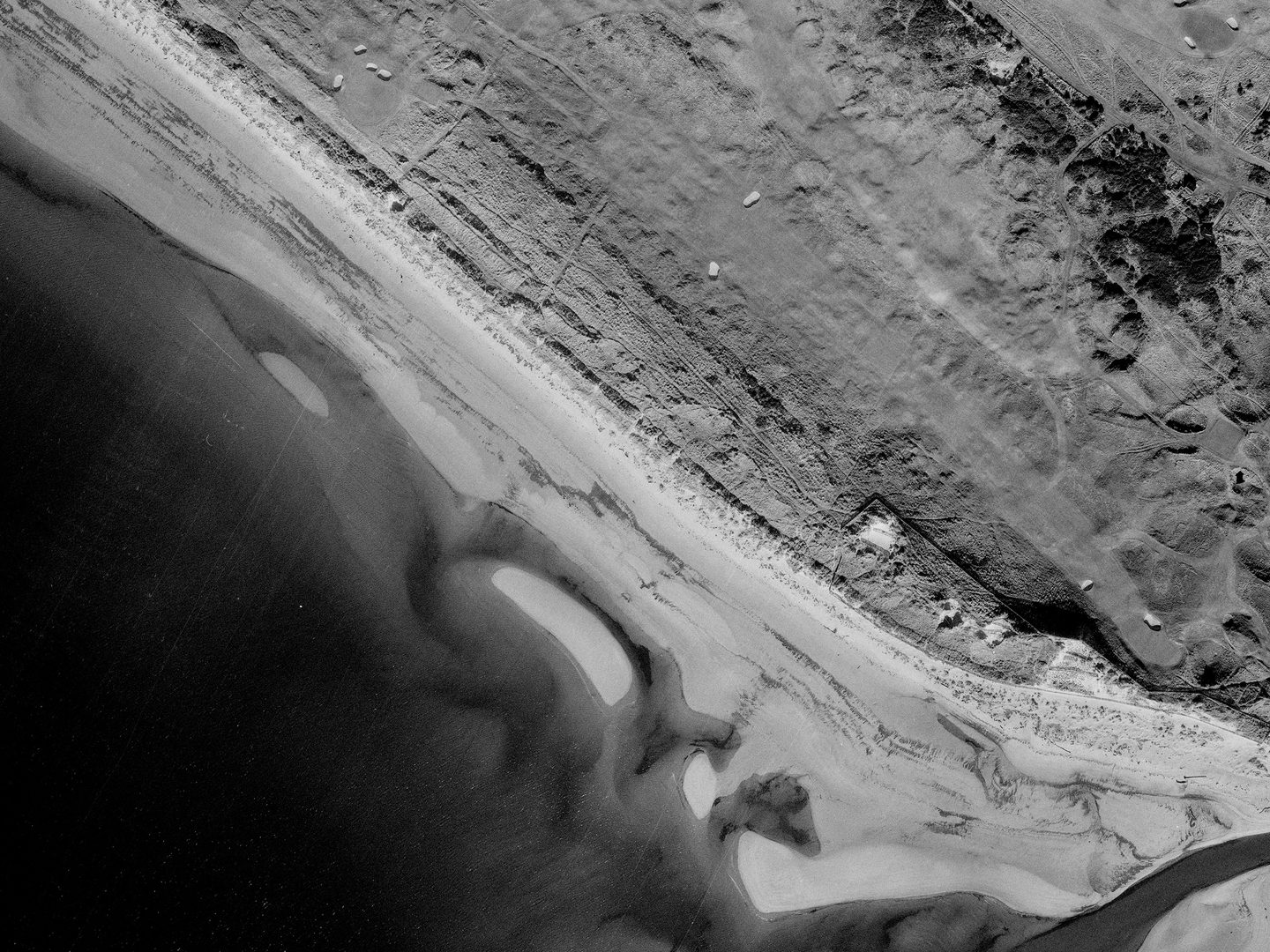 A historic black and white vertical aerial photo of a golf course running along the shore, with focus on a long, straight hole running from top left to bottom right.