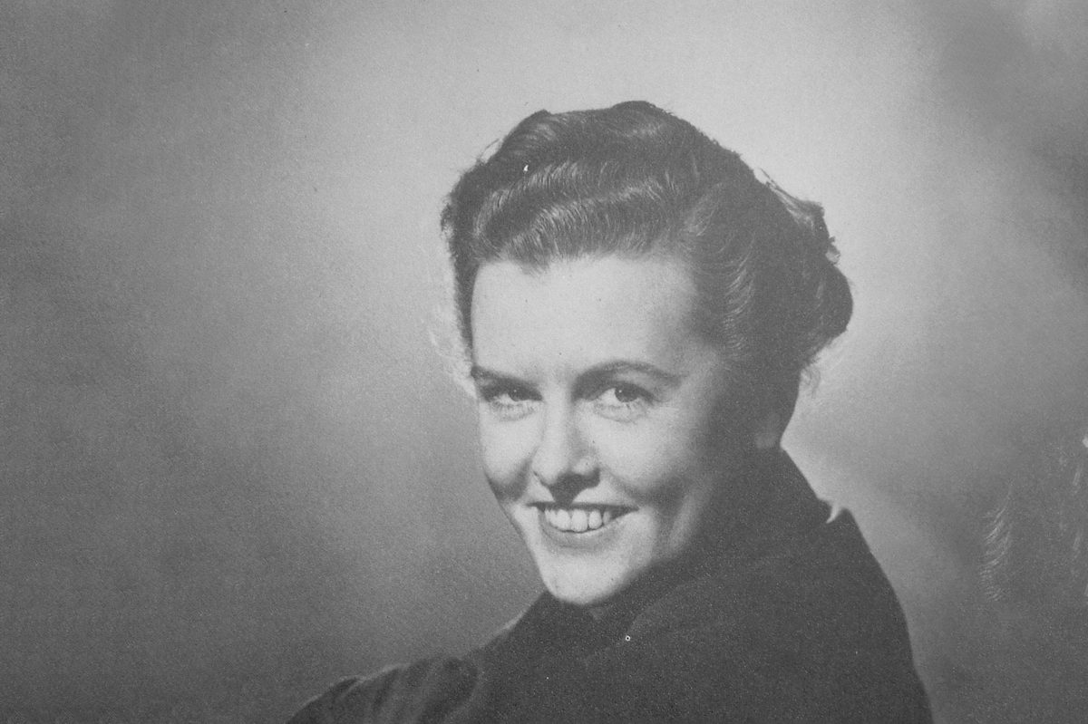 A black and white historic photo of a woman smiling at the viewer over her left shoulder.