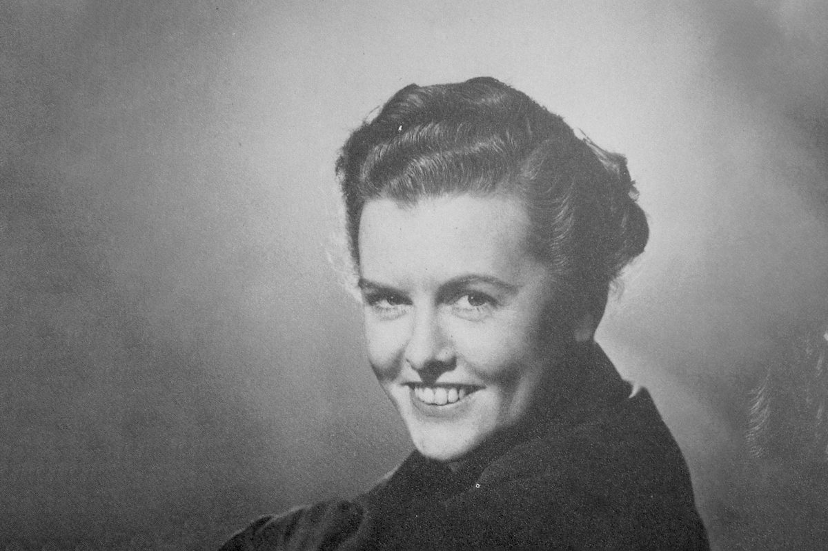 A black and white historic photo of a woman smiling at the viewer over her left shoulder.