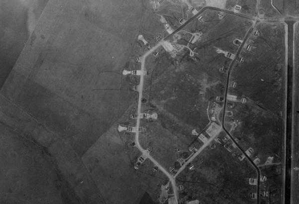 A black and white aerial photo of 17 planes at an airfield. The planes are all situated in bays off two tracks running vertically through the image – one light-coloured and one dark. The planes and tracks are surrounded by featureless fields.