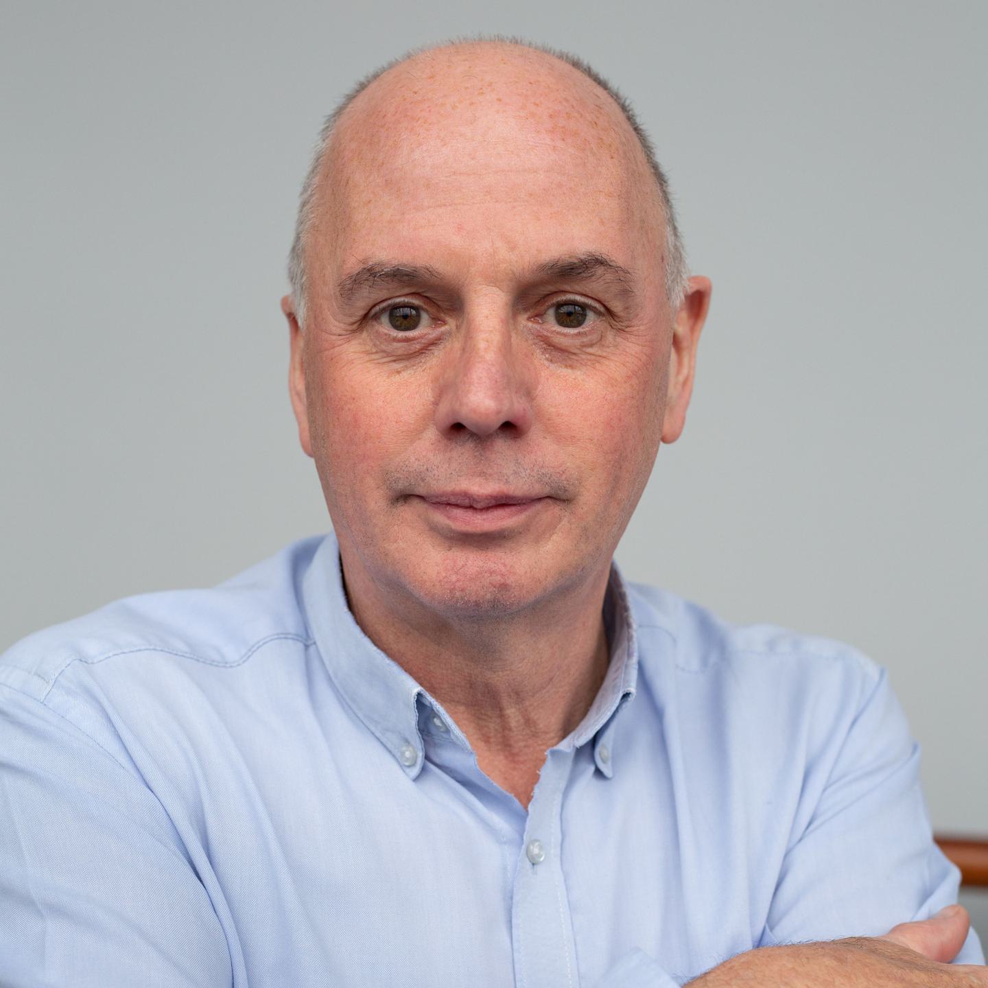 A head-and-shoulders view of a man with white skin and short grey hair, wearing a light blue shirt.